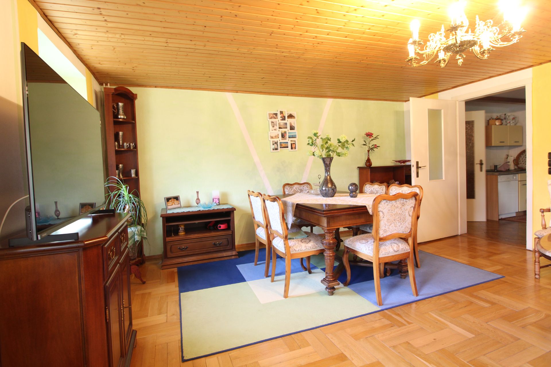 Esszimmer mit Holztisch, sechs Stühlen, Kronleuchter, Holzboden und grün gestrichener Wand.