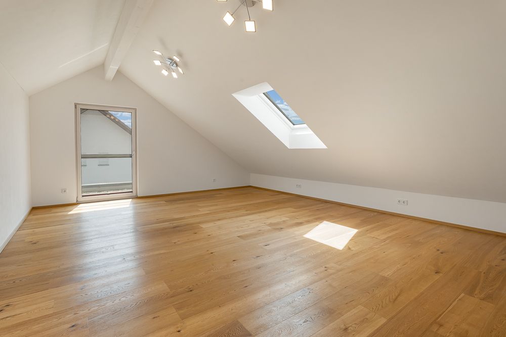 Leerer, heller Dachgeschossraum mit Schrägdecke, Holzfußboden und Dachfenster.