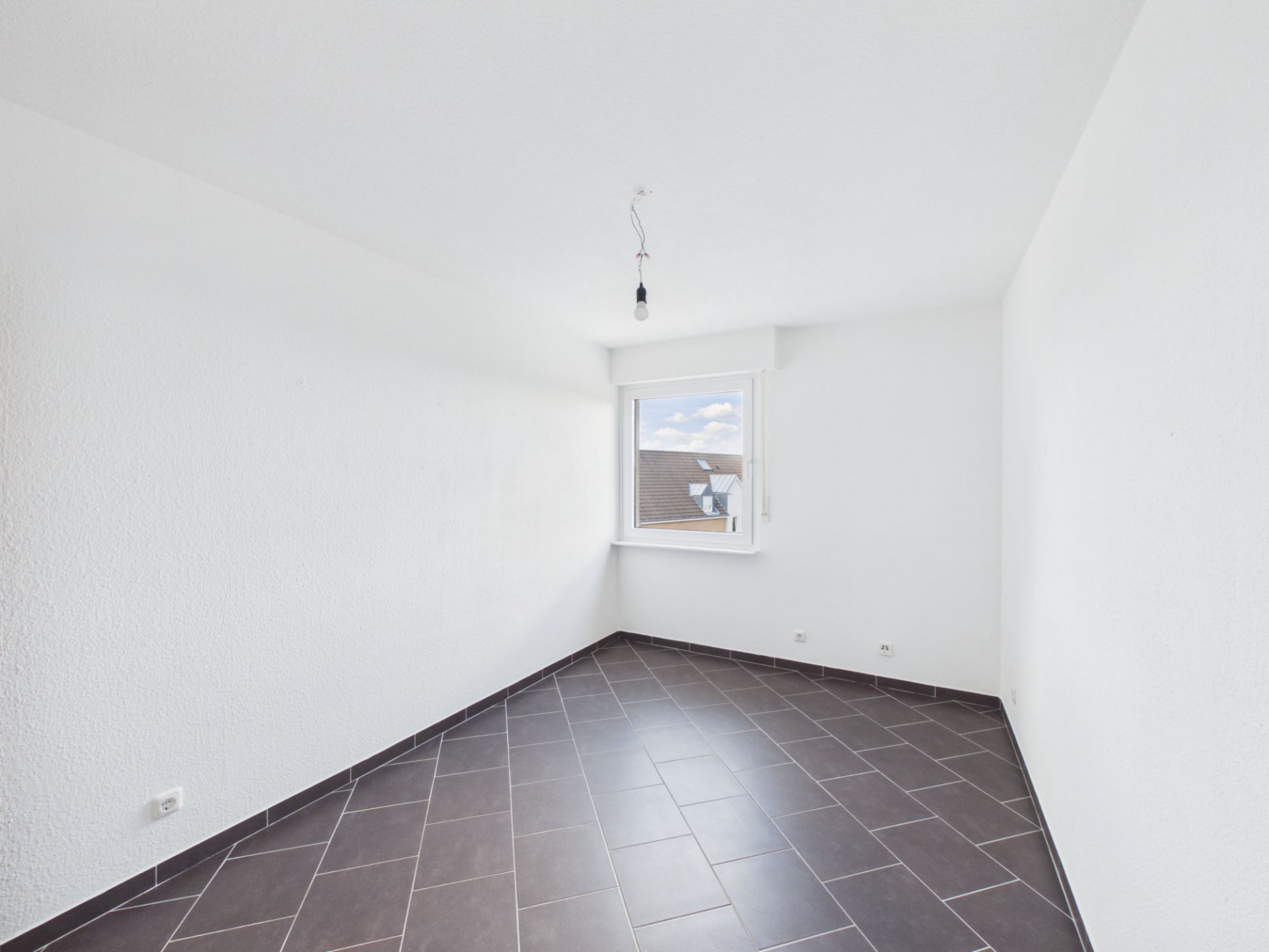 Leeres Zimmer mit weißen Wänden, dunklem Boden und einem Fenster.