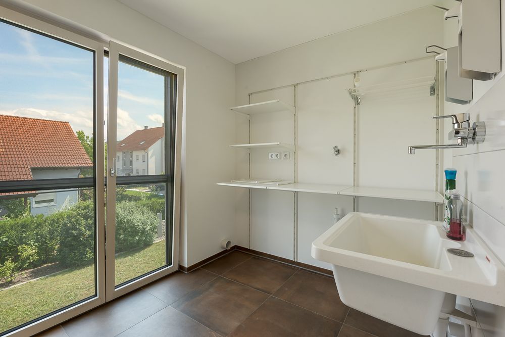 Heller Hauswirtschaftsraum mit großem Fenster, Waschbecken und weißen Regalböden an der Wand.