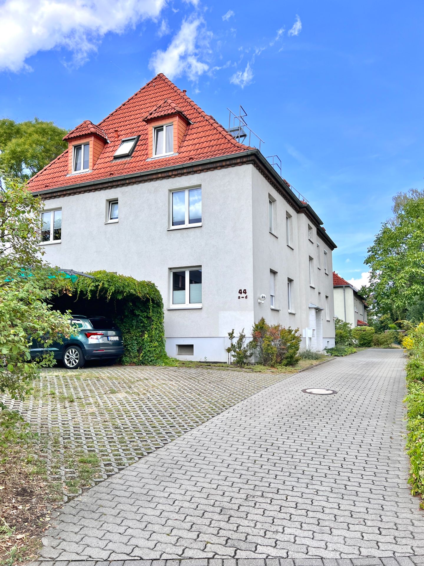 Weißes Wohnhaus mit rotem Dach, Einfahrt und parkendem Auto unter Carport.