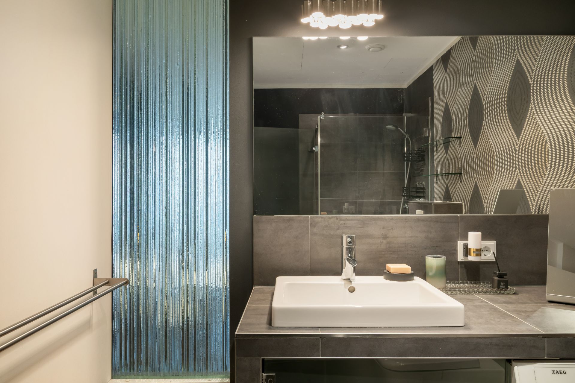 Modernes Badezimmer mit Waschbecken, Spiegel, gemusterten Fliesen und Glaswand.