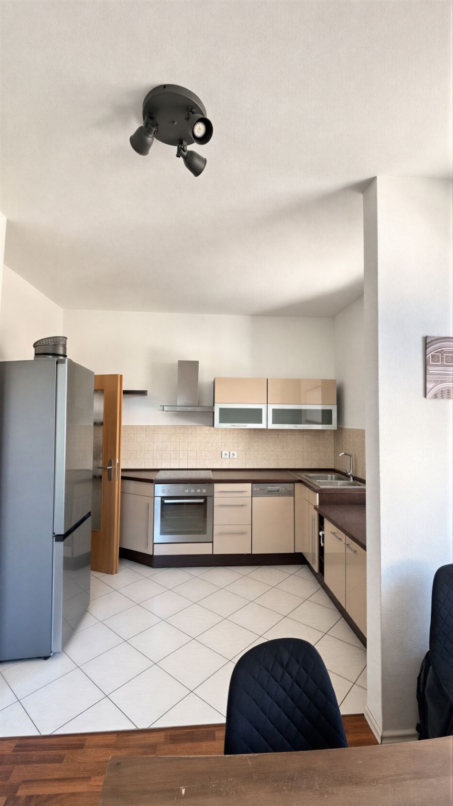 Moderne Einbauküche mit Kühlschrank, Backofen, Spüle und Esstisch mit zwei Stühlen.
