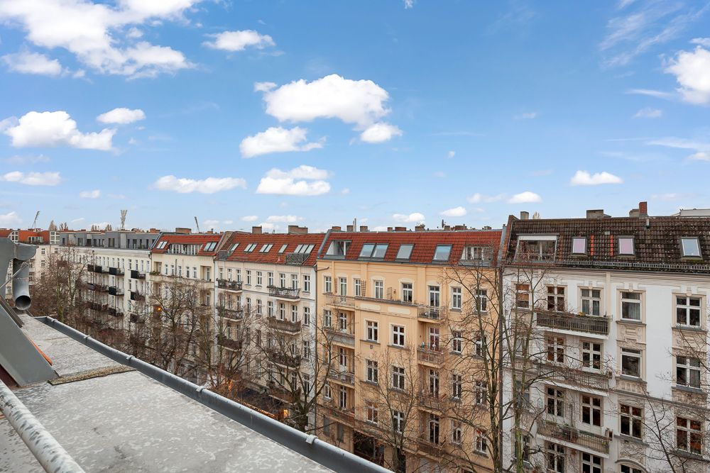 Blick von einem Balkon auf mehrere mehrstöckige Wohnhäuser mit roten Dächern und Bäumen davor.