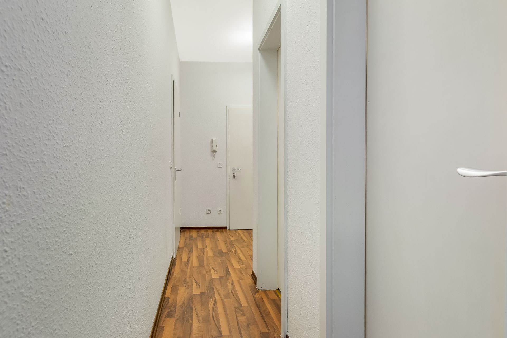 Heller Flur mit Holzboden, weißen Wänden und mehreren Türen in einer Wohnung.