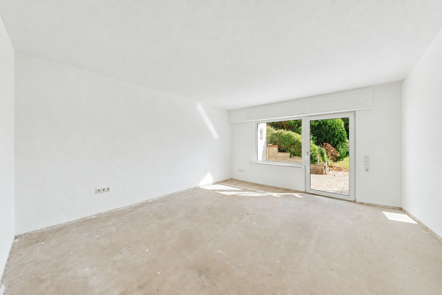 Leerer, heller Raum mit weiß gestrichenen Wänden und großer Glastür zum Garten.
