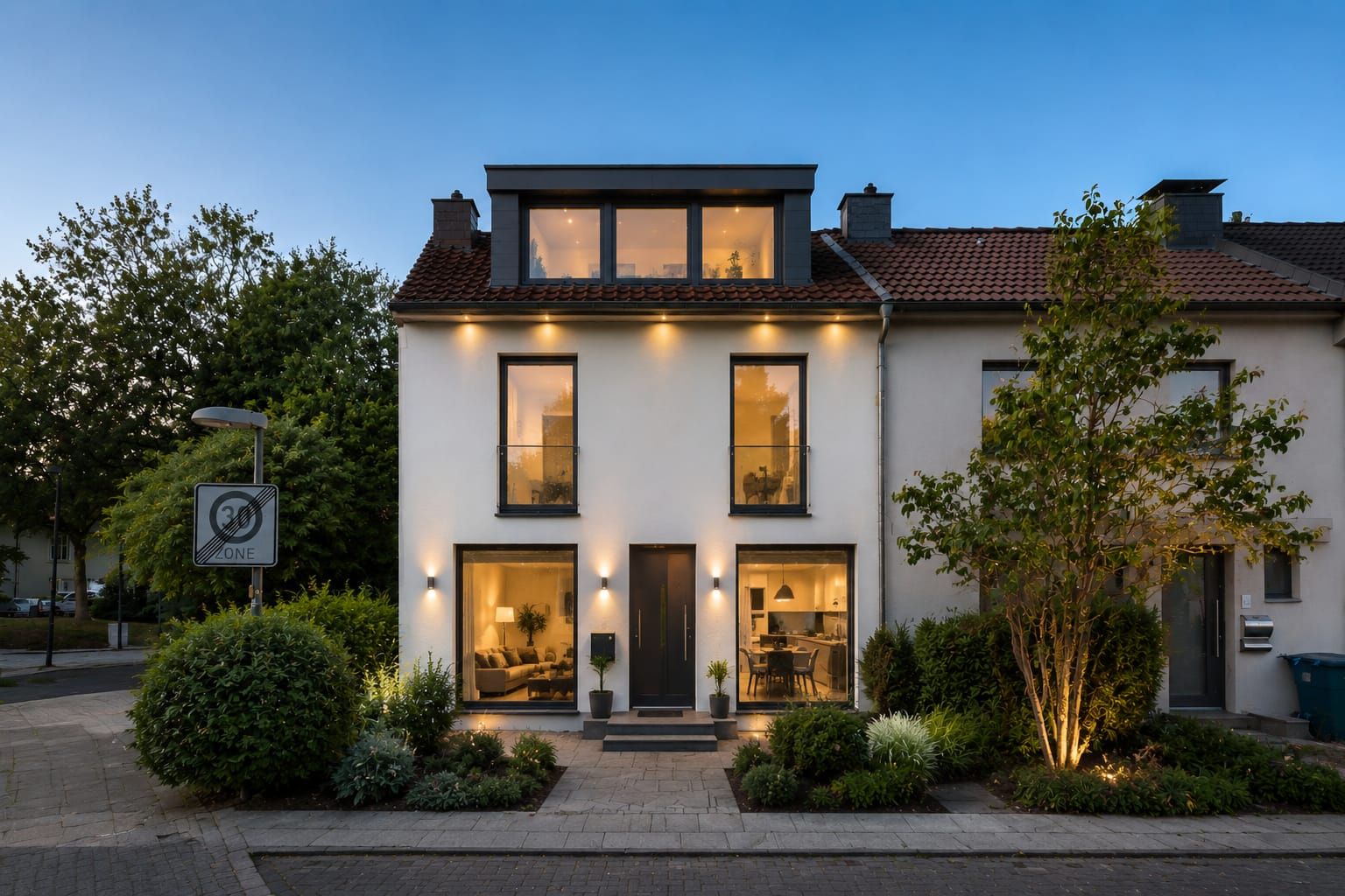 Modernes zweistöckiges Wohnhaus mit großen beleuchteten Fenstern und Vorgarten am Abend.