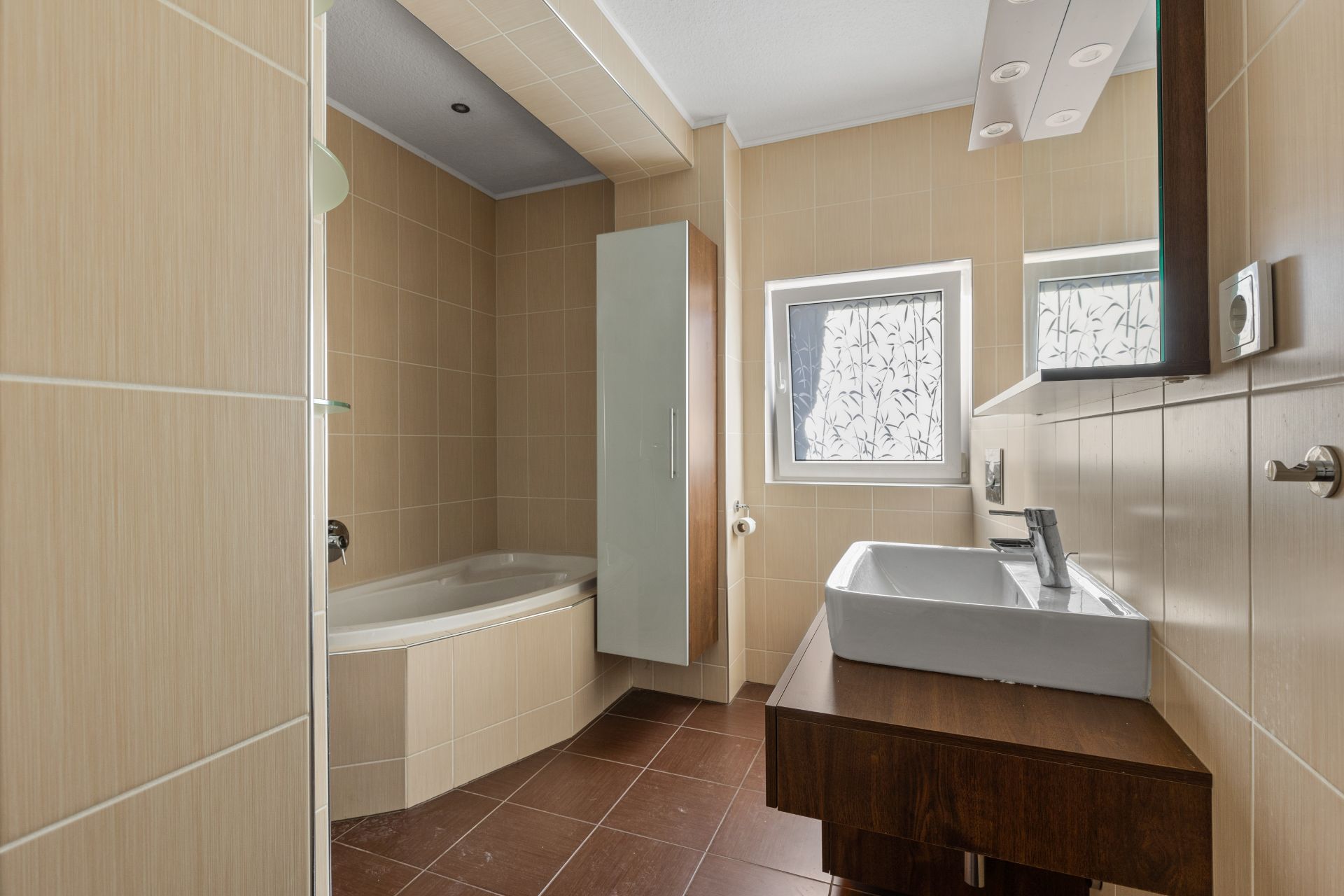 Modernes Badezimmer mit Eckbadewanne, Waschbecken, großem Spiegel und zwei Fenstern.