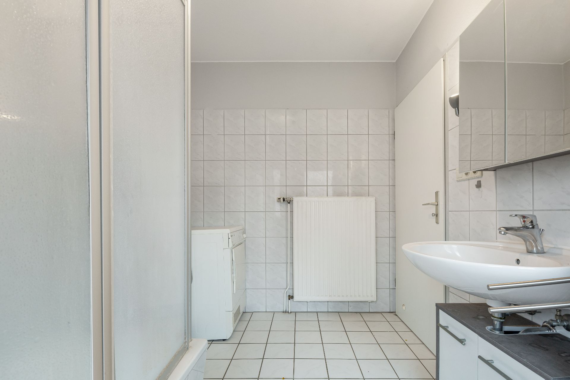 Helles Badezimmer mit Waschbecken, Spiegel, Heizung und Fliesenboden.