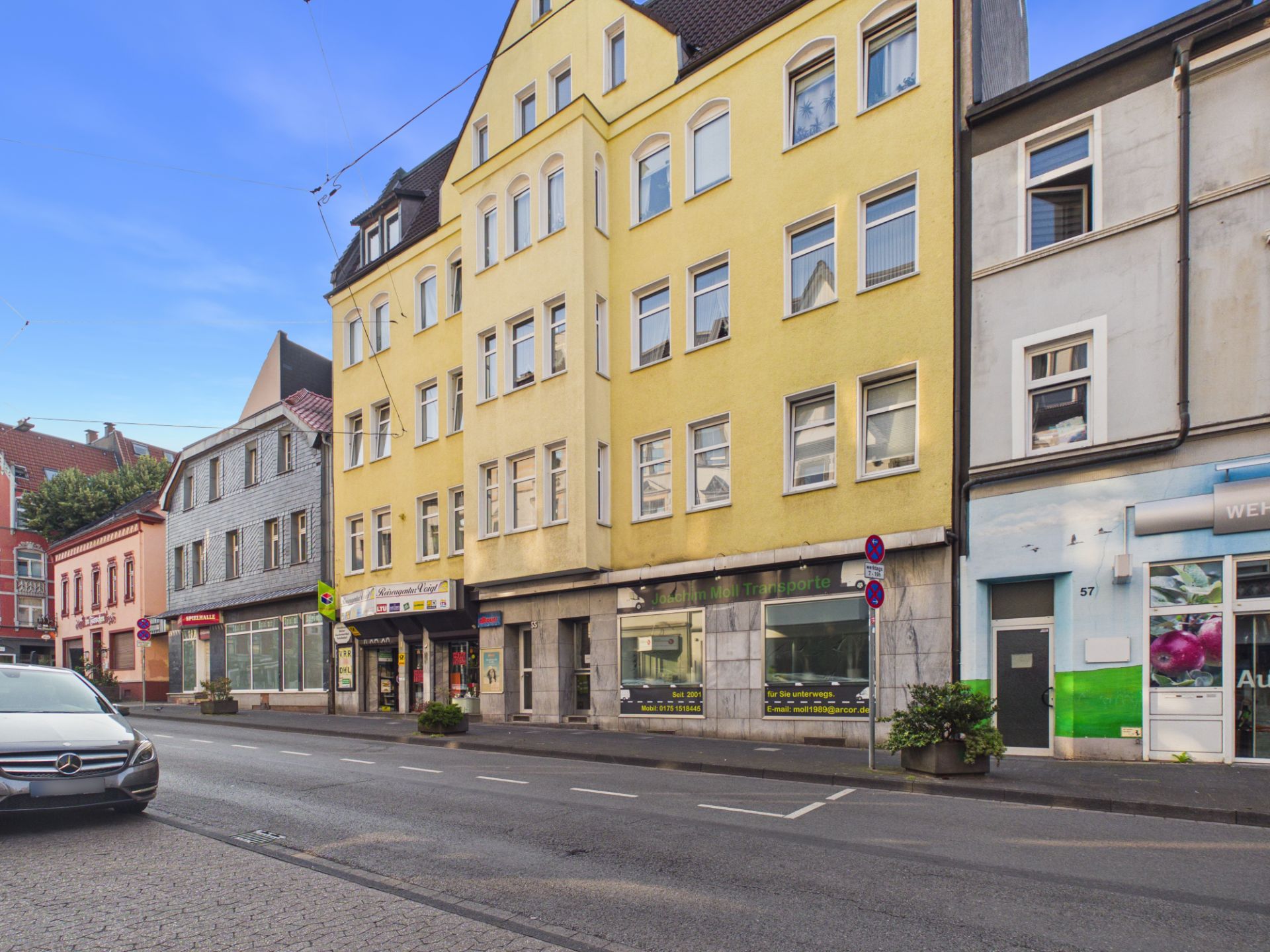 Mehrstöckiges gelbes Wohnhaus mit Geschäften im Erdgeschoss an einer Straße.