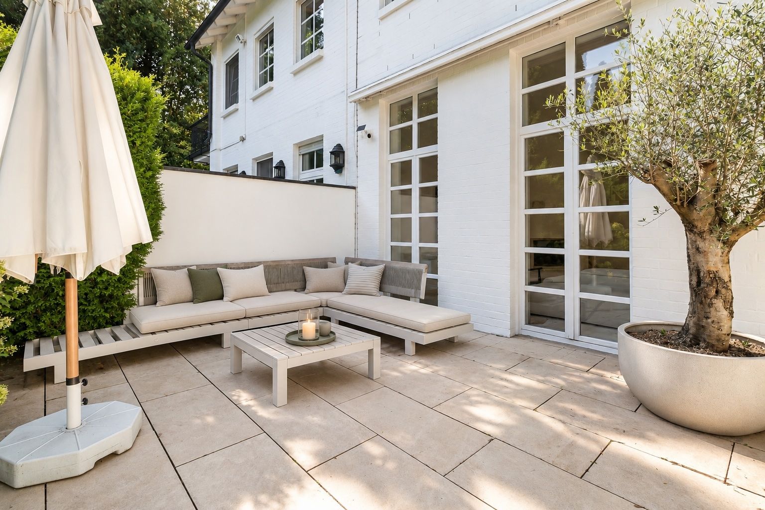 Helle Terrasse mit Ecksofa, Couchtisch, Sonnenschirm und Baum in großem Topf.