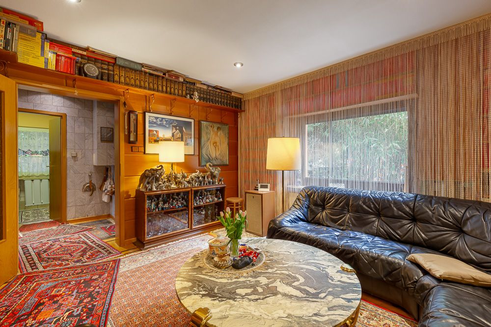 Gemütliches Wohnzimmer mit schwarzem Ledersofa, rundem Tisch, Lampen und vielen Büchern im Regal.