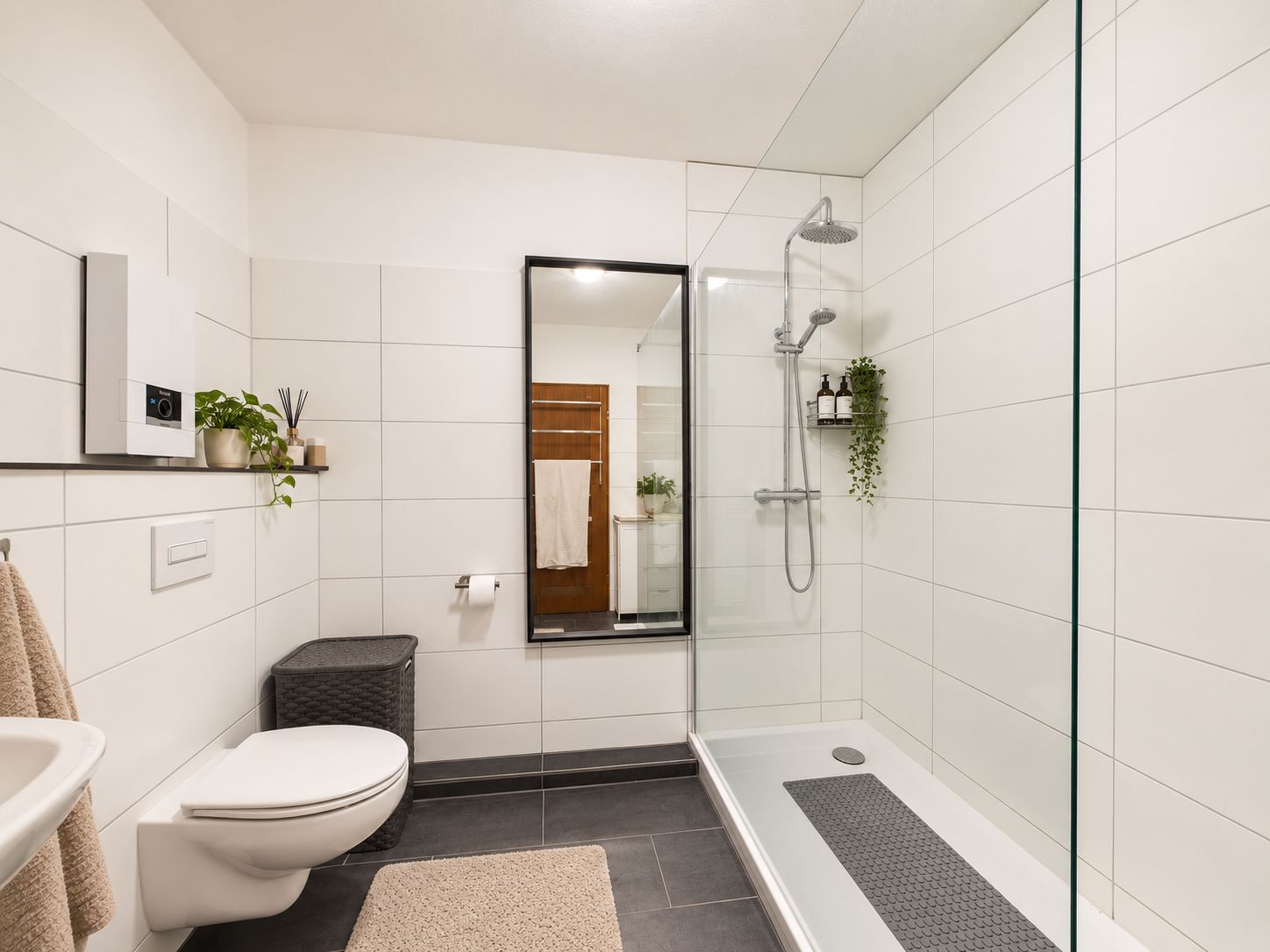 Modernes Badezimmer mit bodengleicher Dusche, WC, Waschbecken, Spiegel und Pflanzen.