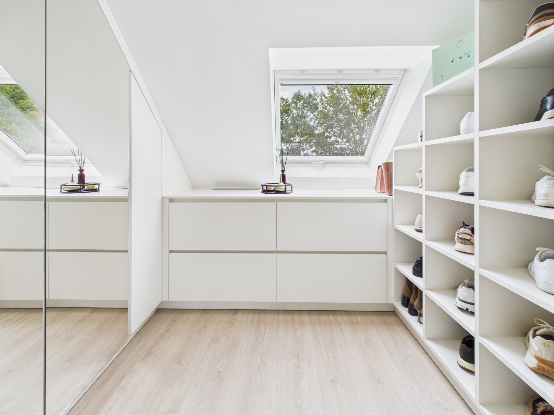 Heller Ankleideraum mit weißen Schränken, Regalen für Schuhe und Dachfenstern.