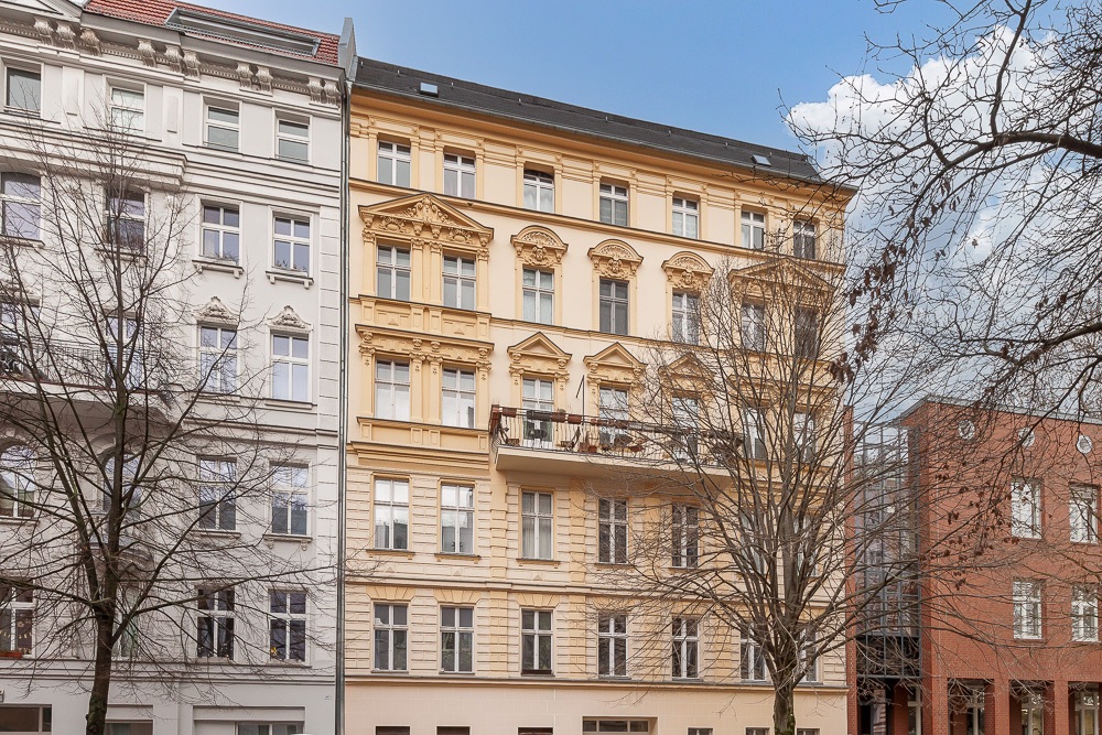 Mehrstöckiges Wohnhaus mit gelber Fassade und Balkonen, davor kahle Bäume.