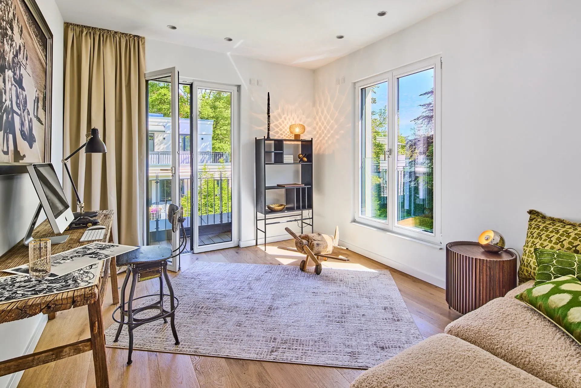 Helles Arbeitszimmer mit Schreibtisch, Sofa, Regal und Zugang zum Balkon.