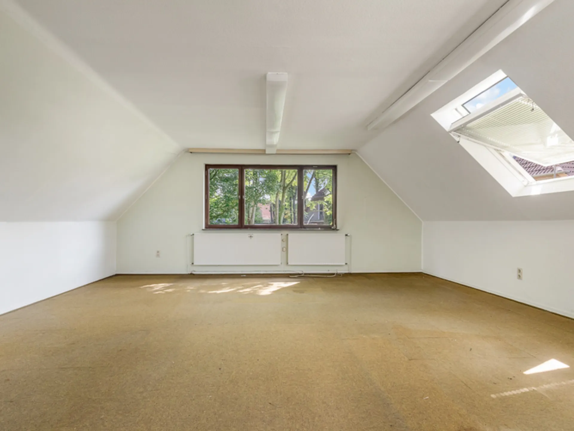 Leerer Dachraum mit schrägen Wänden, Teppichboden, großem Fenster und Dachfenster.