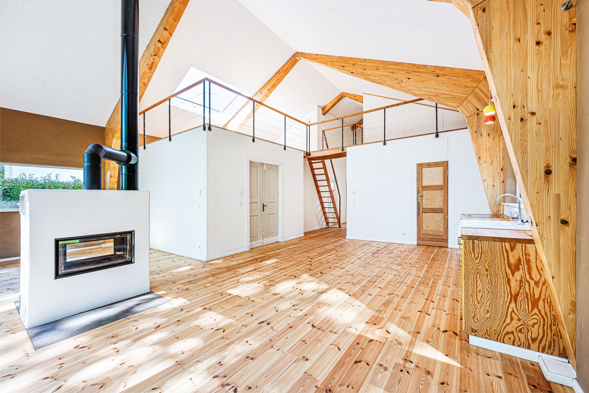 Helles Wohnzimmer mit Kamin, Holzfußboden, Küche und offener Galerie mit Treppe.