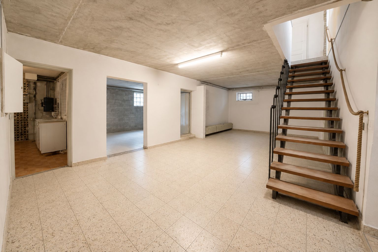 Heller Kellerraum mit Fliesenboden, Holztreppe und mehreren Türen zu Nebenräumen.