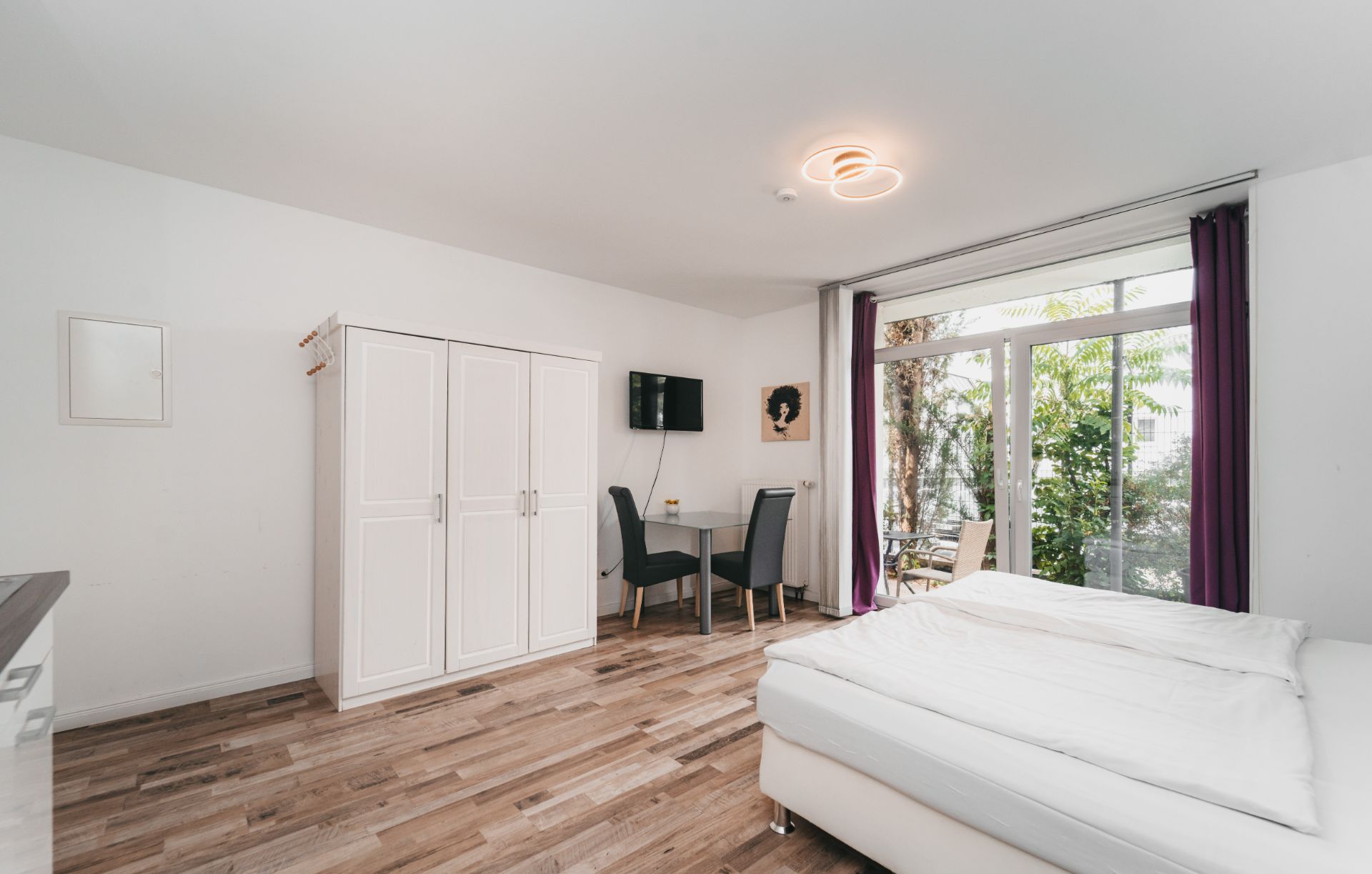 Helles Schlafzimmer mit Bett, Kleiderschrank, Schreibtisch und großem Fenster mit Blick ins Grüne.
