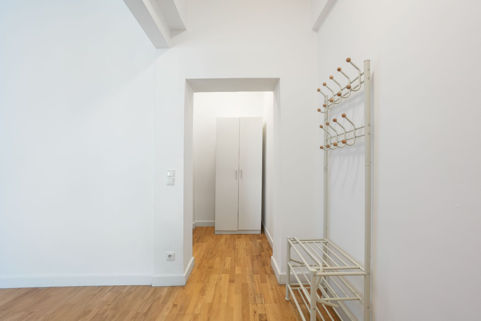 Flur mit Holzfußboden, Garderobenständer und weißem Schrank im Hintergrund.