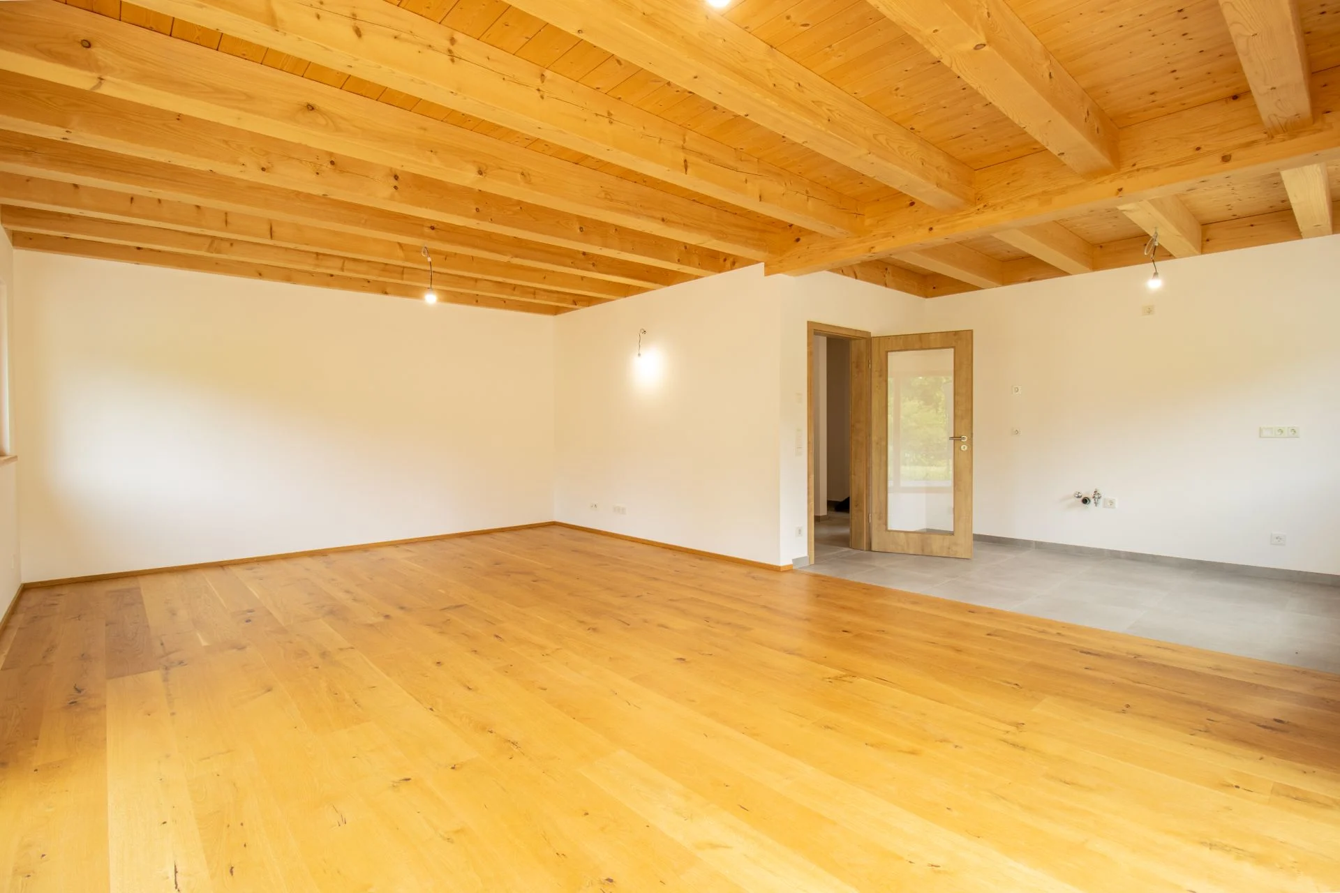 Leerer Raum mit Holzdecke, Holzboden und einer Glastür auf der rechten Seite.