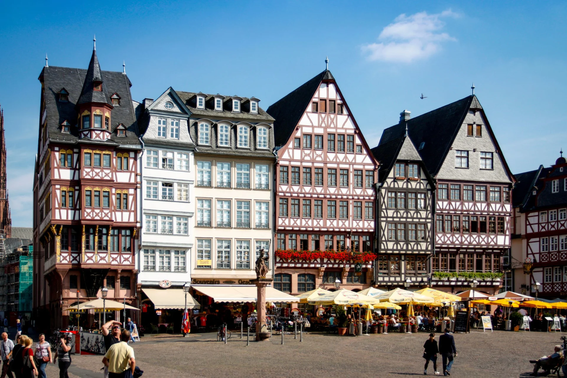 Mehrere Fachwerkhäuser mit spitzen Dächern und Cafés vorne auf einem Platz.