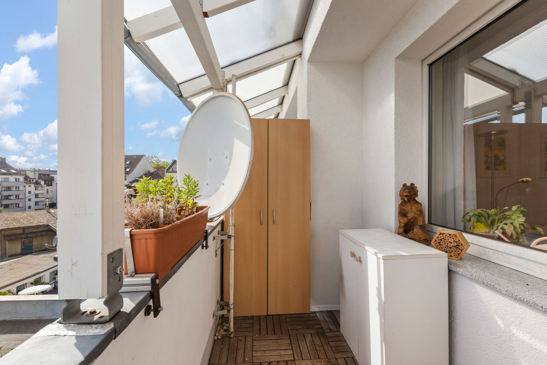 Überdachter Balkon mit Pflanzkasten, Satellitenschüssel, Schrank und Dekoration.