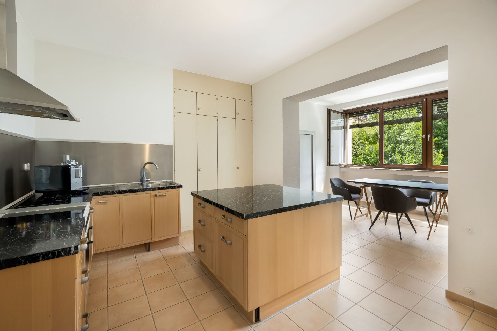 Moderne Küche mit Kochinsel, hellem Boden und Essbereich am Fenster.