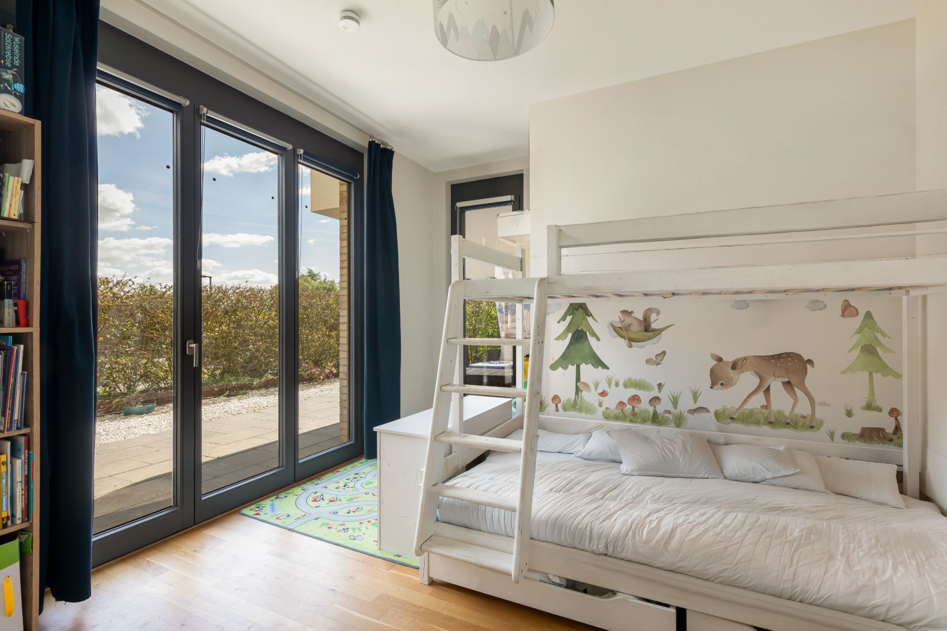 Kinderzimmer mit Etagenbett, großem Fenster und Wanddeko mit Waldtieren.