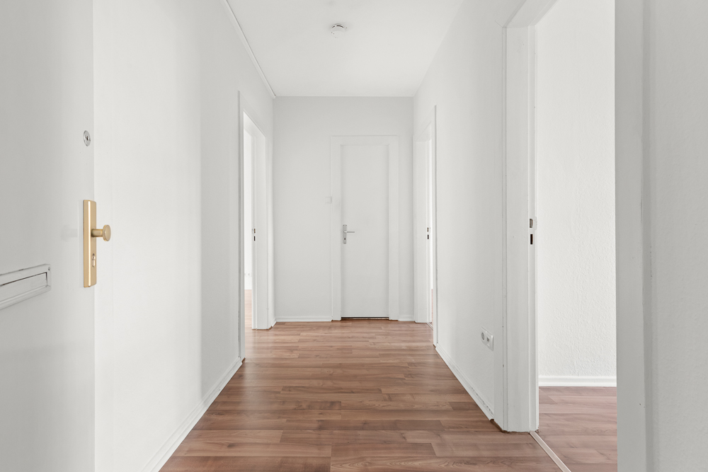 Heller Flur mit weiß gestrichenen Wänden und Holzfußboden, mehrere Türen zu angrenzenden Räumen.