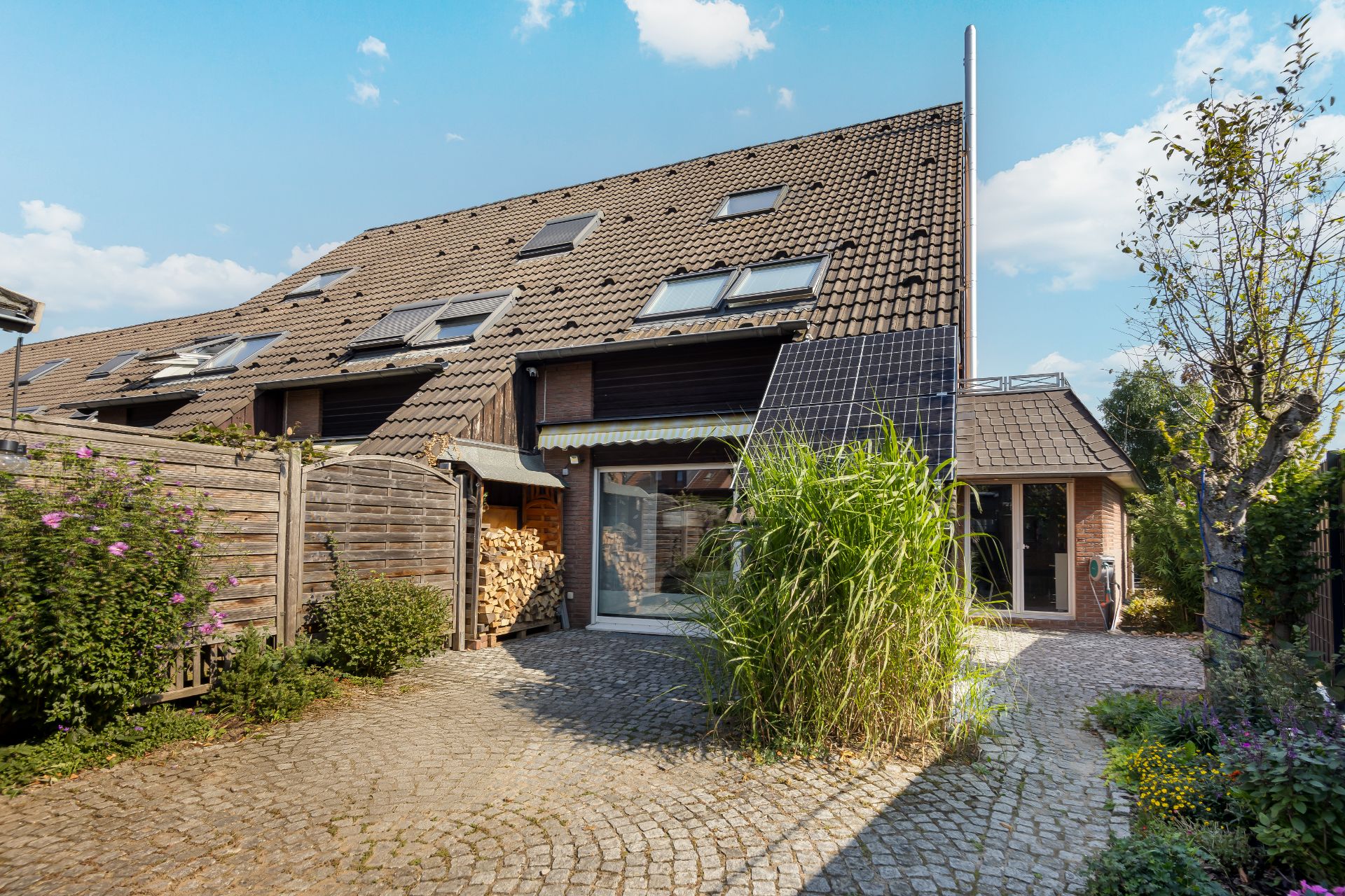 Wohnhaus mit Schrägdach, Solarpanel, großem Fenster und kleinem Hof mit Pflanzen.
