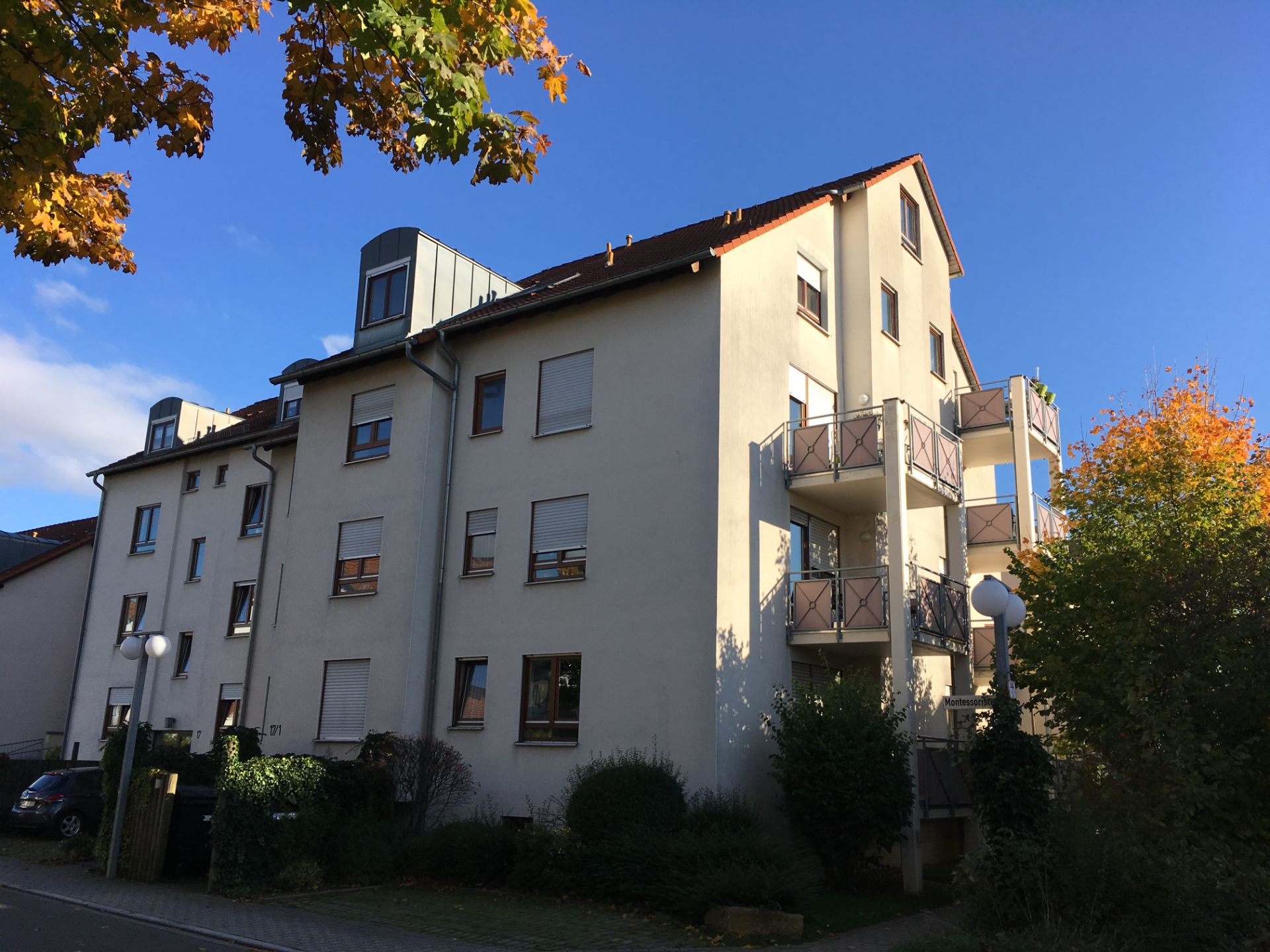 Mehrfamilienhaus mit mehreren Balkonen und einigen Bäumen im Vordergrund.