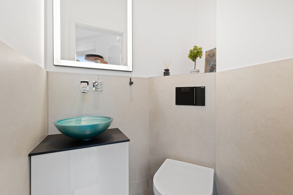 Modernes Badezimmer mit grünem Waschbecken, Toilette, Spiegel und kleiner Pflanze auf einer Ablage.