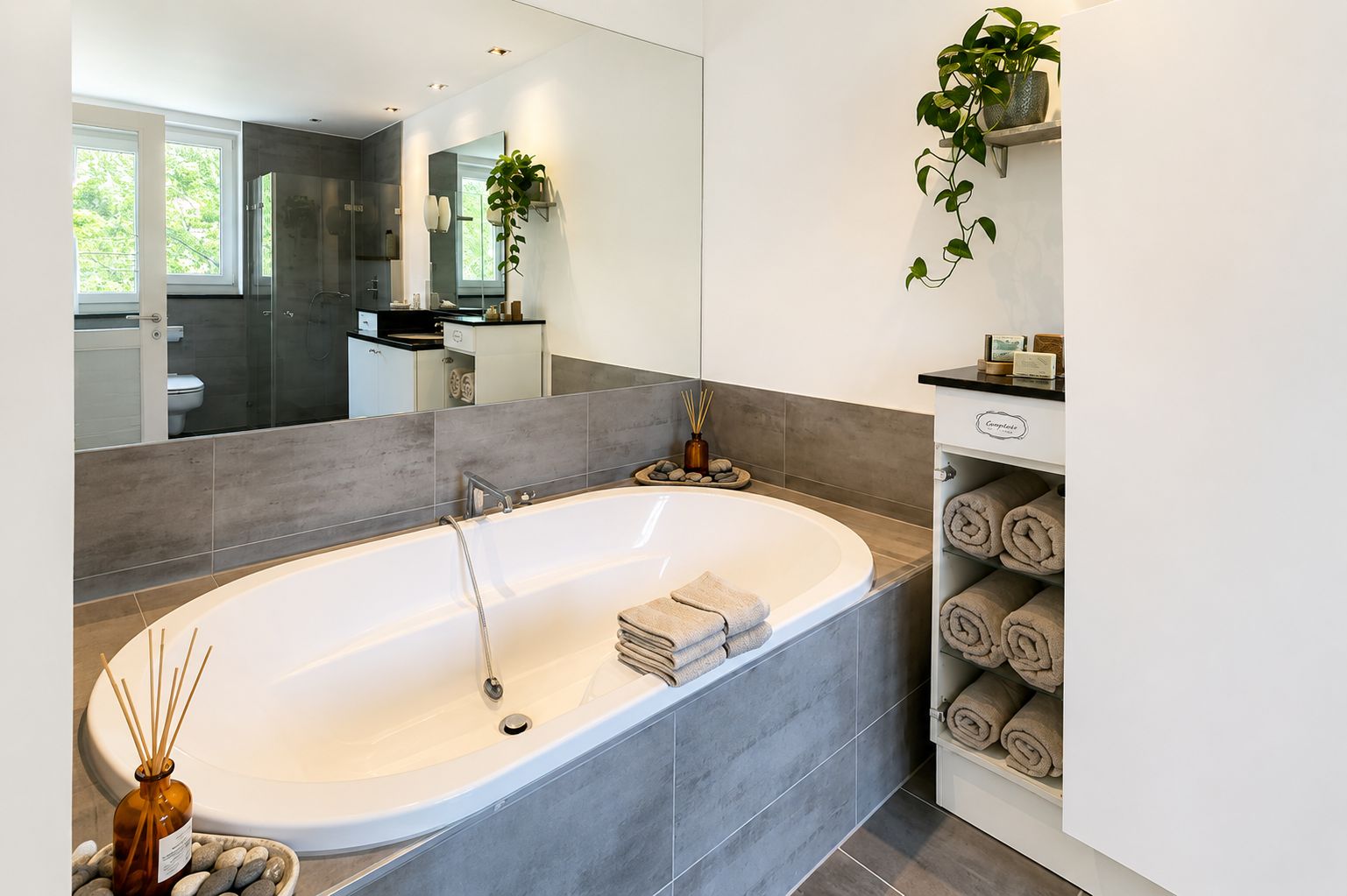 Modernes Badezimmer mit großer Badewanne, Handtüchern, Pflanzen und Spiegel.