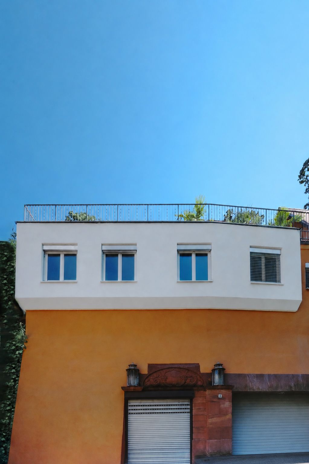 Fassade eines Wohnhauses mit orangefarbenem Erdgeschoss, weißen Fenstern und Garagentoren.