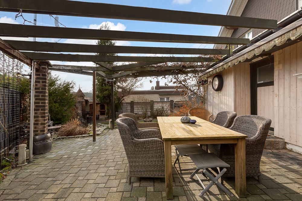 Überdachte Terrasse mit Holztisch und Korbstühlen im Garten eines Wohnhauses.
