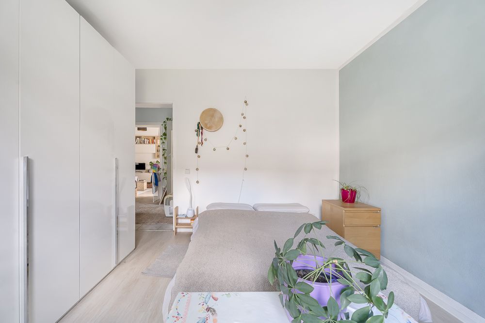 Helles Schlafzimmer mit Doppelbett, Pflanzen, Kleiderschrank und Kommode.