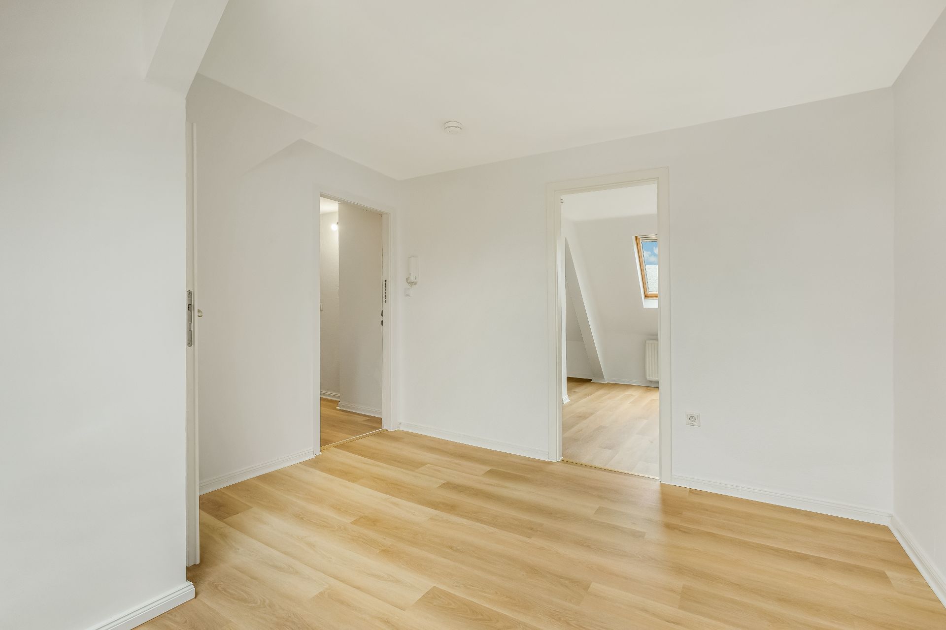 Heller Raum mit Holzfußboden, weißen Wänden und zwei offenen Türen zu weiteren Zimmern.