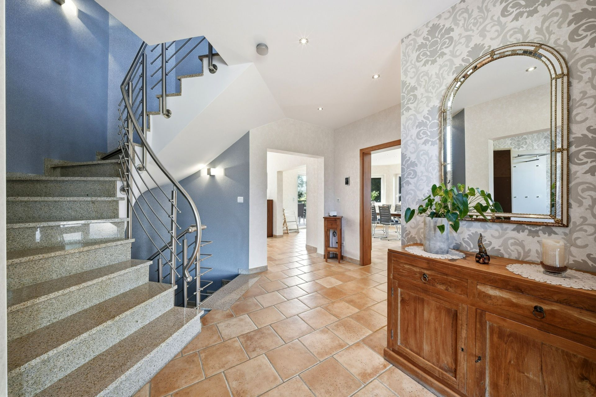 Heller Flur mit Treppe, Fliesenboden, Holzkommode und großem Spiegel.