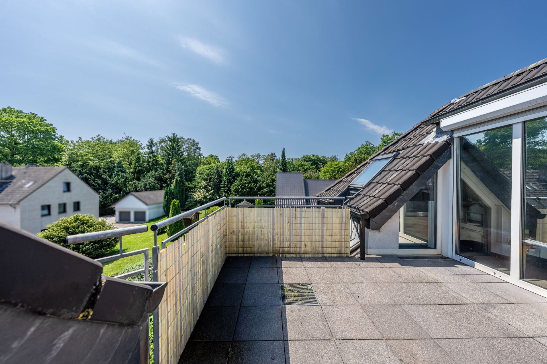 Großer Balkon mit Fliesenboden und Blick auf Gärten und Nachbarhäuser bei klarem Himmel.