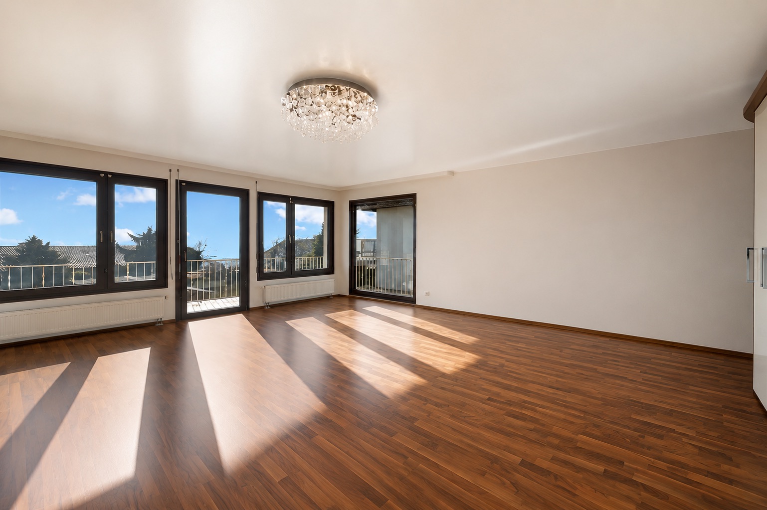 Helles Wohnzimmer mit Holzfußboden, großen Fenstern und Kronleuchter.