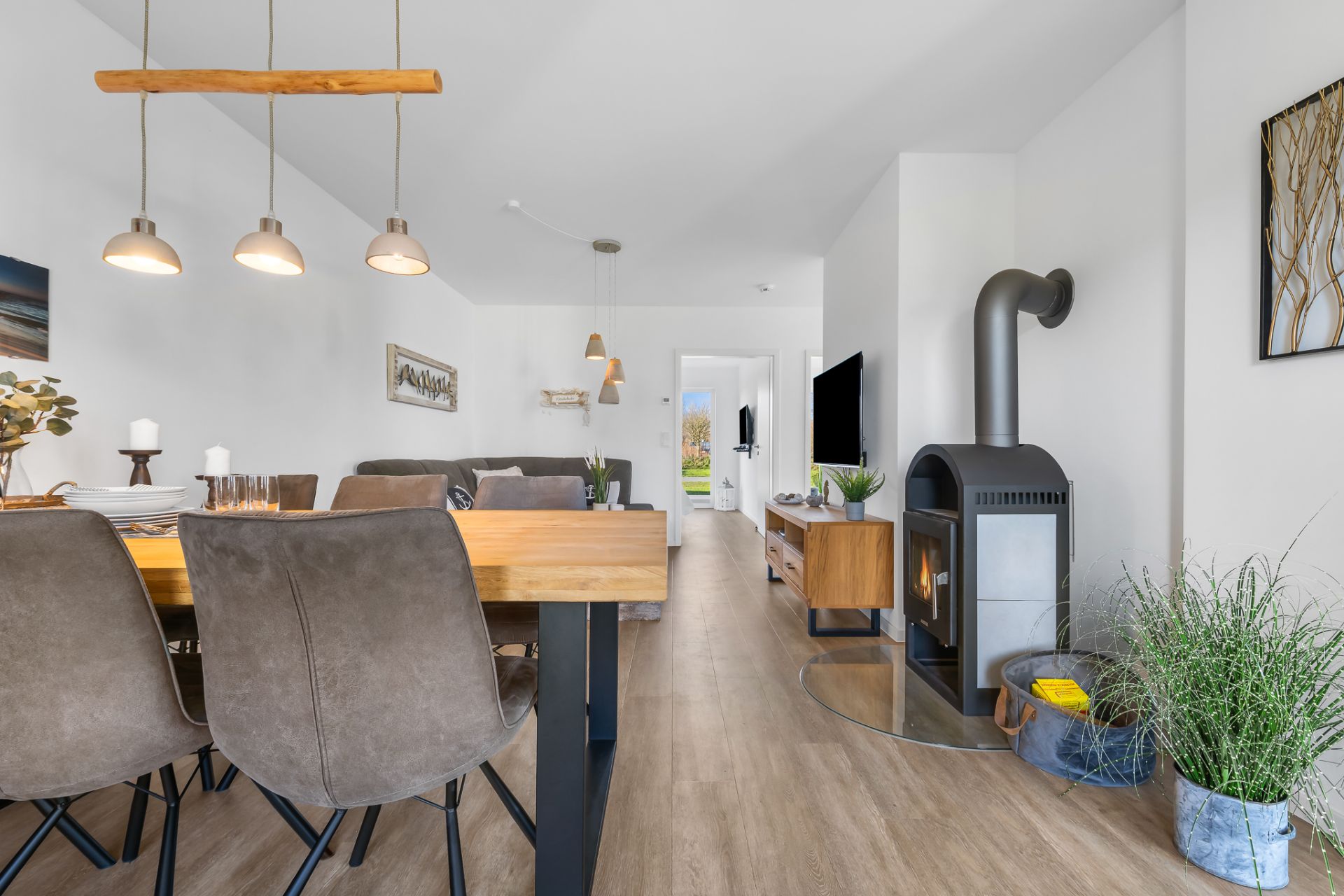 Helles Wohnzimmer mit Esstisch, Stühlen, Holzofen, Fernseher und modernen Lampen.