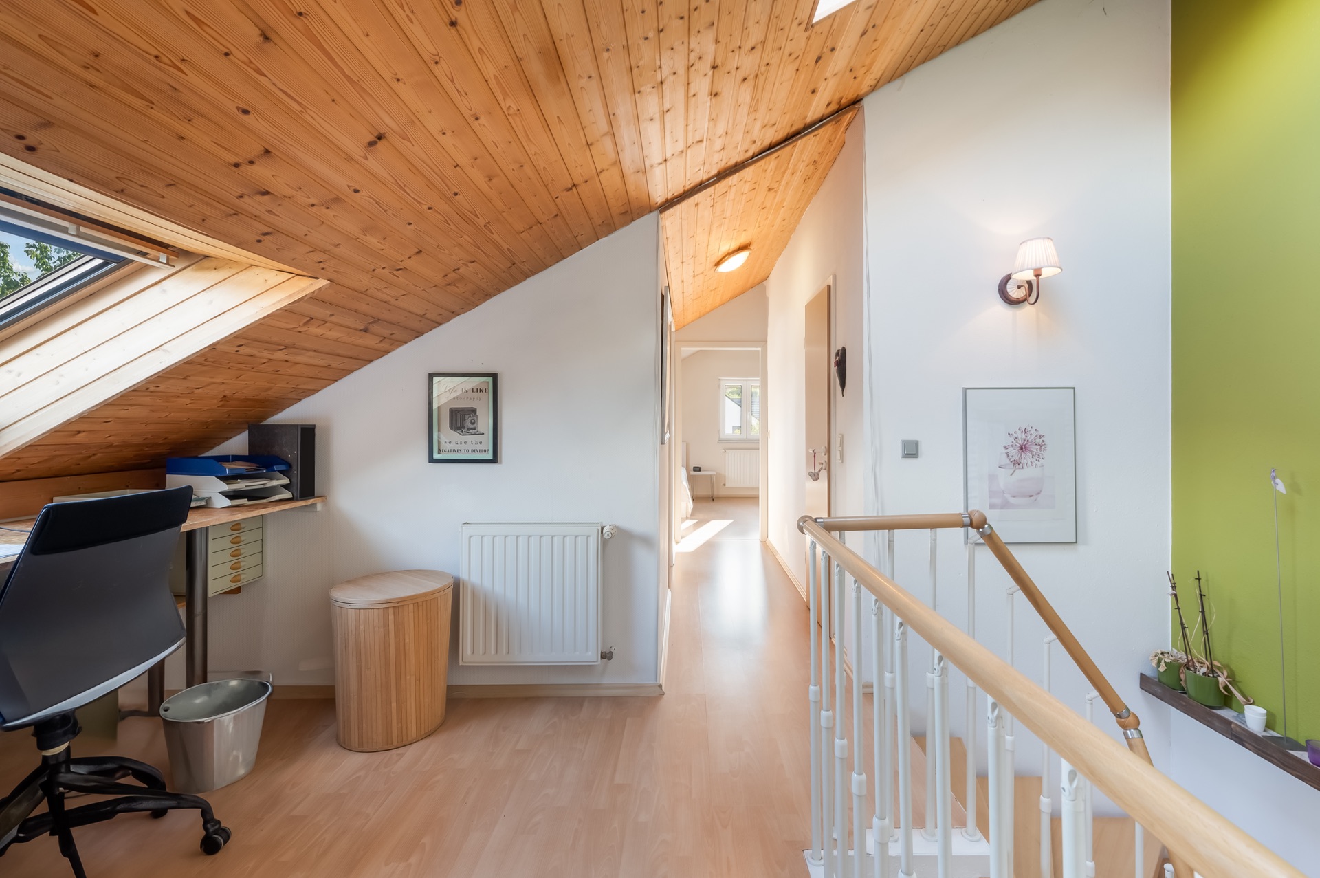 Heller Dachgeschossflur mit Holzdecke, Schreibtisch am Fenster und Treppengeländer.