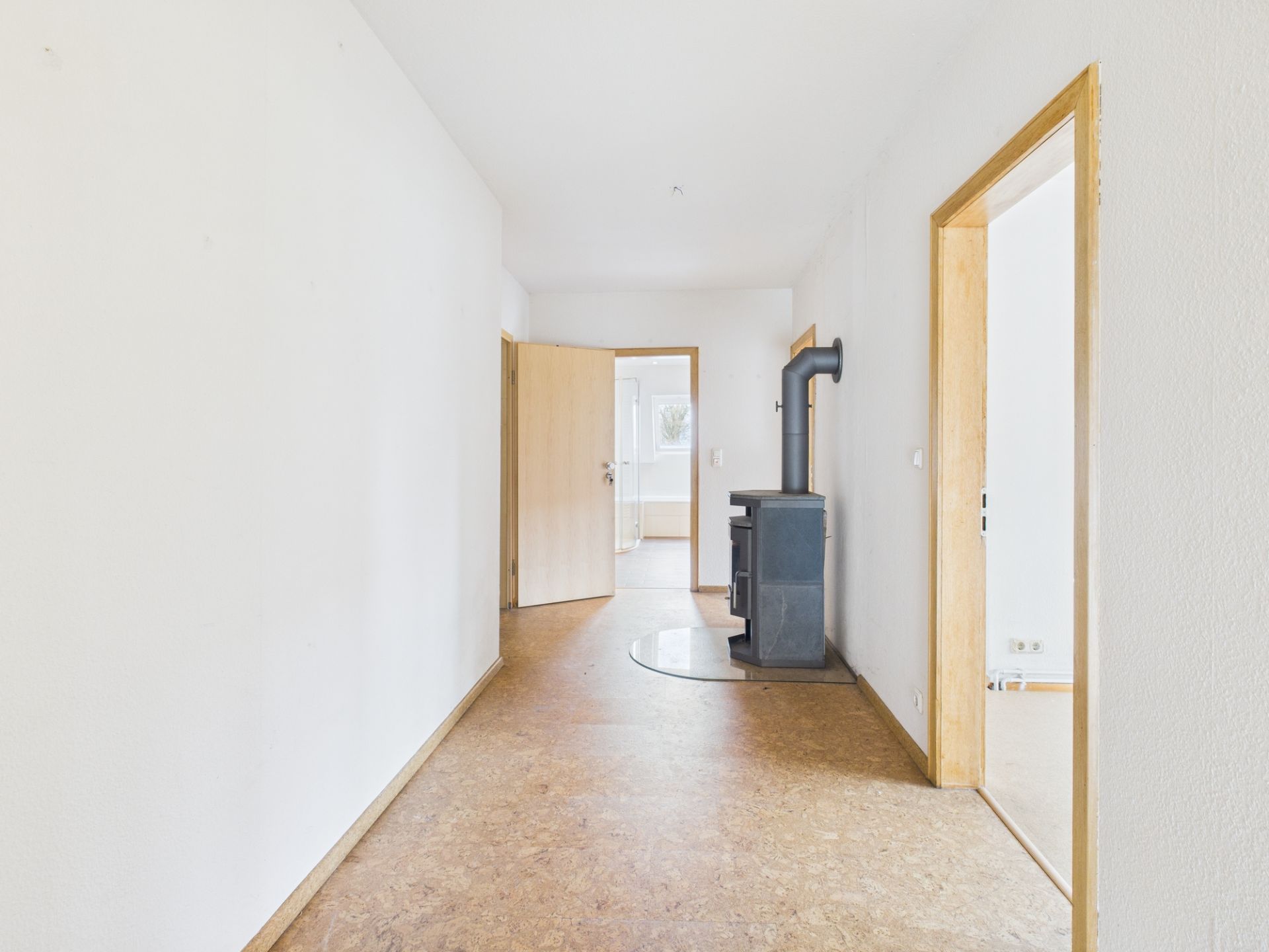 Heller Flur mit Holzofen, offenen Türen und hellem Boden in einem Wohnhaus.