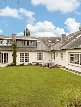 Großes Einfamilienhaus mit Garten, vielen Fenstern und schrägem Dach an einem sonnigen Tag.