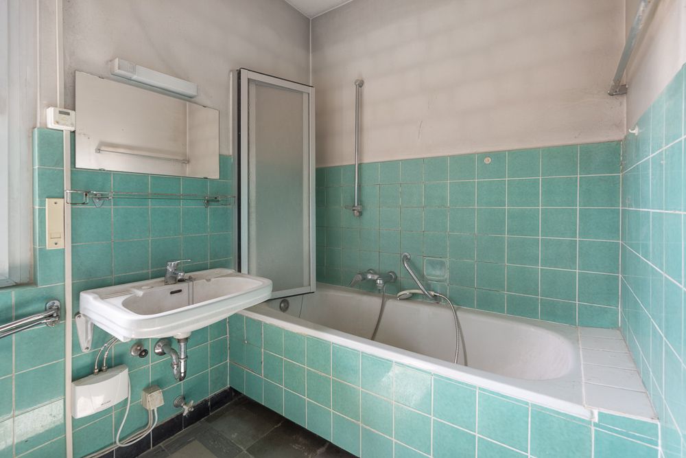 Badezimmer mit grünen Fliesen, Badewanne, Waschbecken und Spiegel.