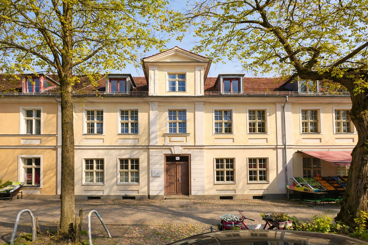 Zweistöckiges Wohnhaus mit hellgelber Fassade, großen Fenstern und Bäumen davor.