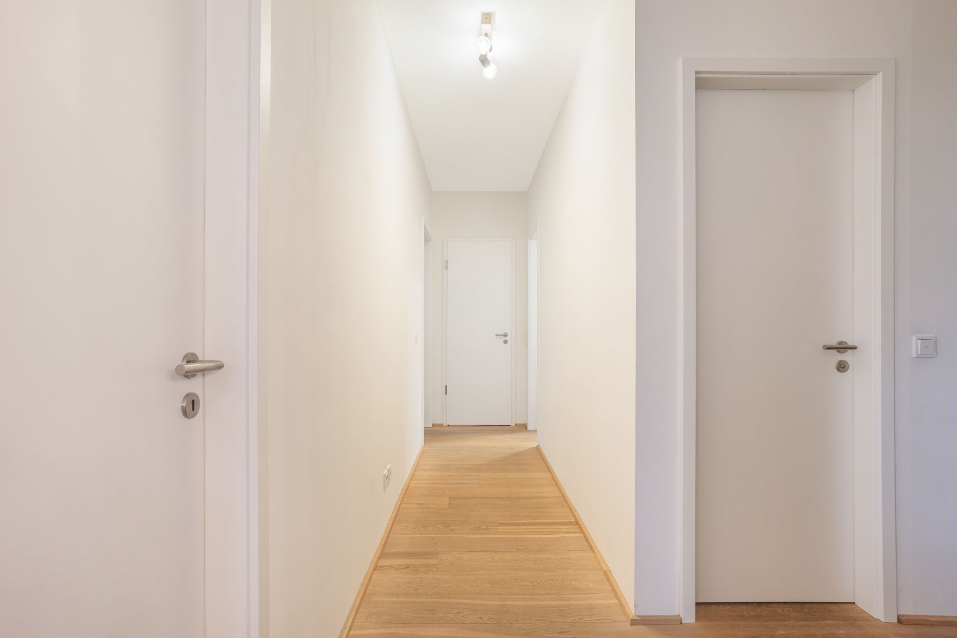 Heller Flur mit Holzboden und mehreren weißen Türen in einer Wohnung.