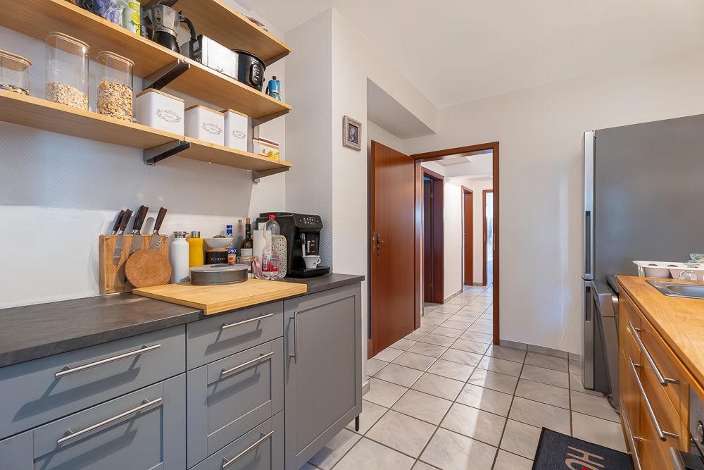 Moderne Küche mit grauen Schränken, offenen Regalen und Küchenutensilien, Flur im Hintergrund.